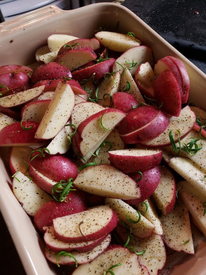 Red potatoes in casserole dish with seasoning ready to be roasted in the oven.