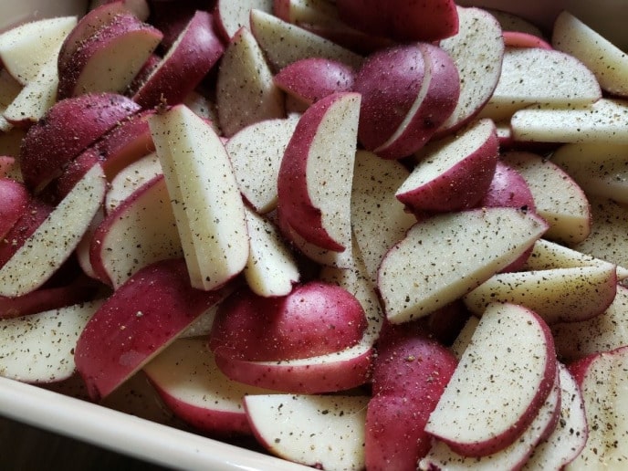Putting seasoning on cut up red potatoes for roasting.