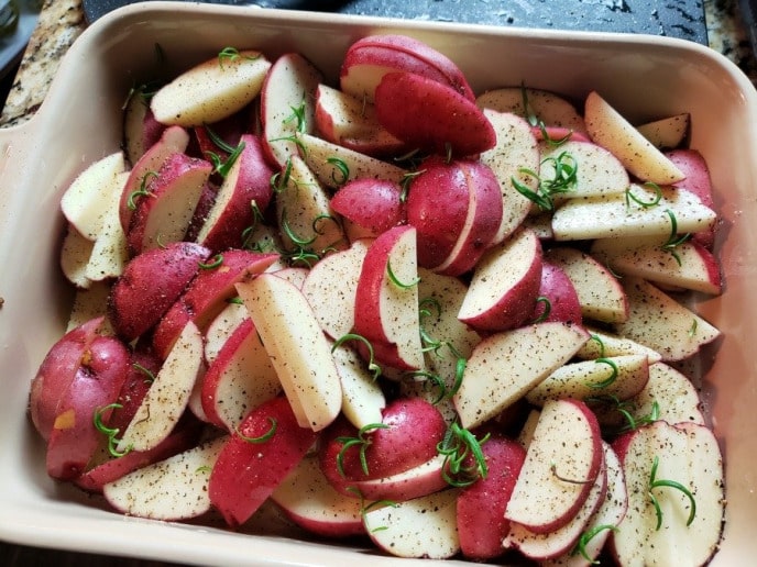 Red potatoes seasoned with salt, pepper, and rosemary, ready to be roasted.