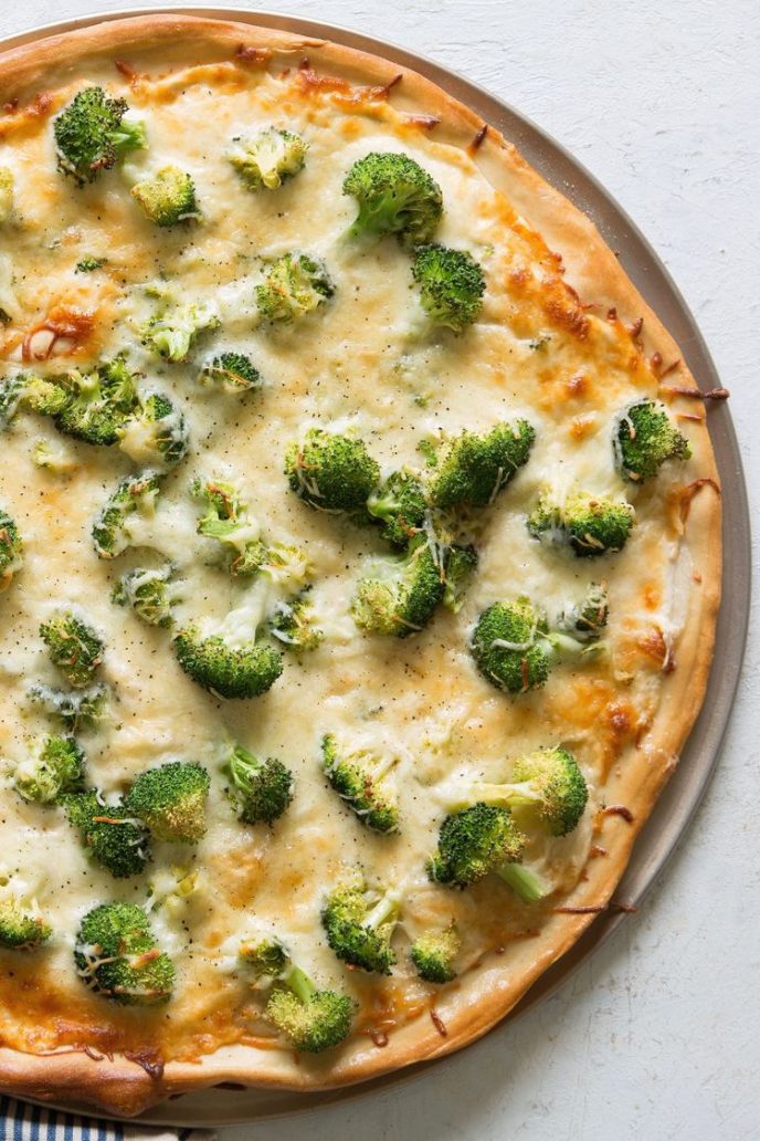 Alfredo Pizza with Chicken recipe on a pizza pan with cheese and broccoli additional pizza toppings.