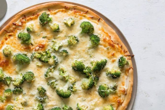 Alfredo pizza recipe cooked with melted cheese, broccoli and chicken on a pizza pan.