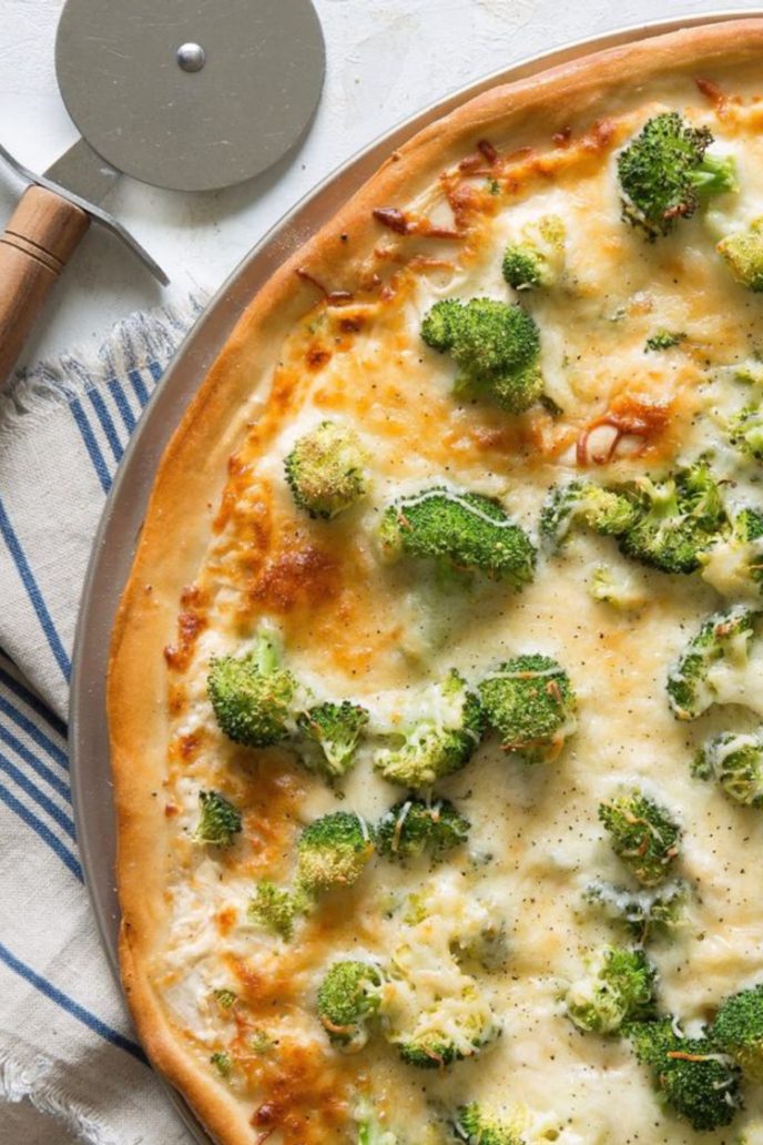 Alfredo pizza with chicken and broccoli cooked on a pizza pan and a pizza cutter sitting next to it