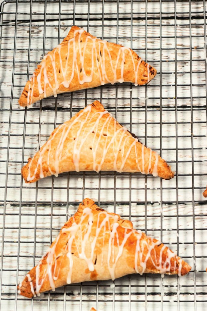 Apple turnovers fresh out of the oven, on a cooling rack and drizzled with icing.
