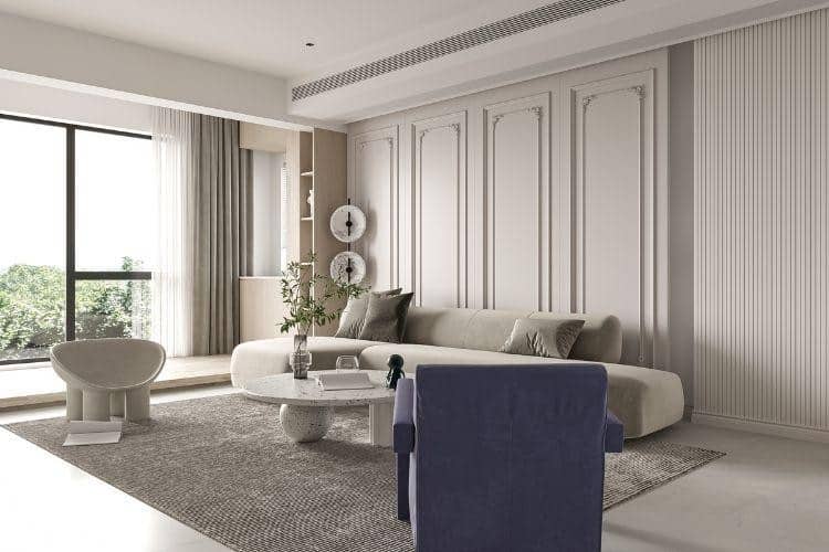 Bright modern living room with a beige sofa, blue armchair, and round coffee table by a large window letting in natural light.