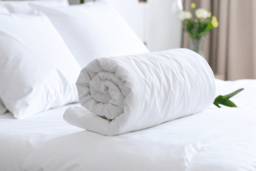 Rolled white duvet on a neatly made bed with white pillows in the background.